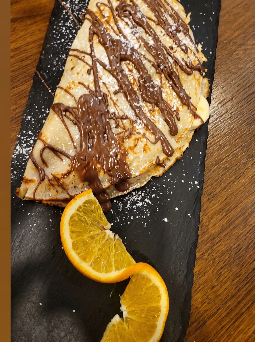 Crêpe mit Schokoladen-Drizzle, Puderzucker und frischen Orangenscheiben